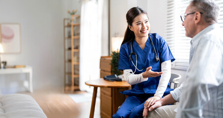 A friendly Asian female nurse in blue scrubs is having a professional and reassuring conversation with a senior male patient.