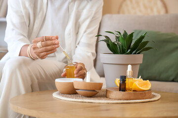 Young woman dropping essential oil into air humidifier on table at home, closeup