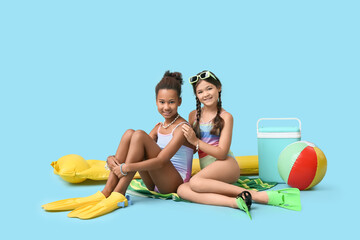 Cute little girls in swimsuits with flippers and beach accessories on blue background © Pixel-Shot