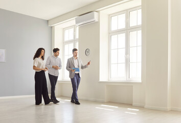 Portrait of young confident man professional realtor standing in empty house with couple clients...