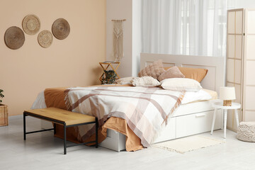 Big comfortable bed and bench near beige wall in interior of bedroom