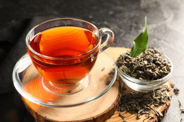 Composition with wooden tray, cup of black tea and bowl of dry leaves on black grunge background, closeup