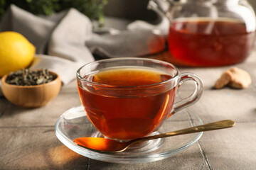 Composition with cup of black tea, teapot and dry leaves on grey tile background, closeup