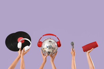 Female hands with disco ball, headphones, vinyl disks and sound speaker on lilac background