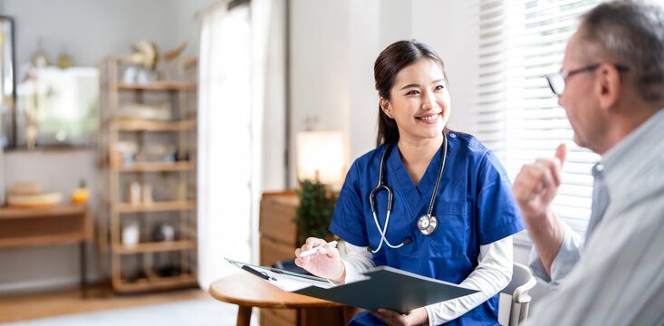 A friendly female nurse in blue scrubs smiles as she consults with an older male patient in a doctor's office or clinic.