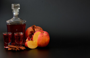 Apple-pomegranate liqueur with cinnamon and anise on a black background, homemade alcohol in a crystal decanter and two shot glasses.