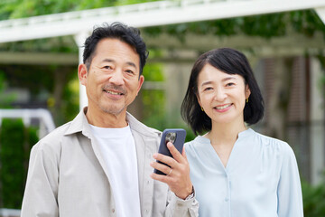 中年の夫婦　スマートフォンを持つ　屋外
