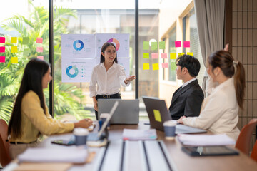 Asian businesswoman leading meeting with team in modern office using sticky notes and charts