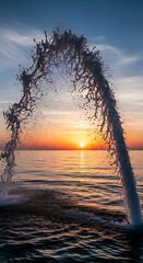 A dramatic water fountain erupts in an arch, spraying a beautiful mist into the air, against the backdrop of a breathtaking sunrise over the calm sea.