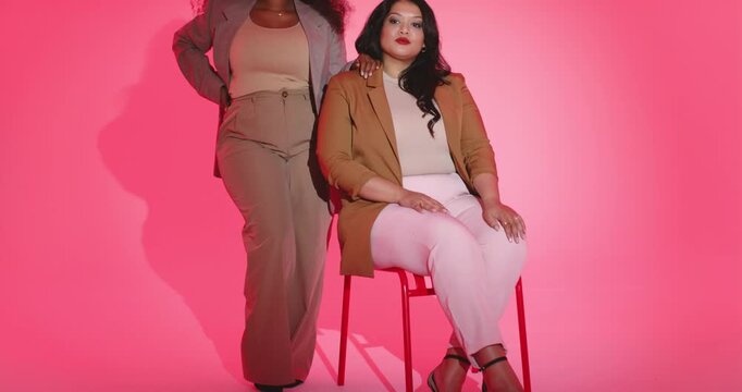 Revealing Diverse female colleagues modeling taupe suit, camel blazer on red stool in studio