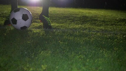 A Nighttime Soccer Player Kicking a Ball on a Grass Field in the Glare of Stadium Lights - Powered by Adobe