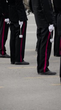 Close-up view of a marching band drumline standing at attention on asphalt, black uniforms with magenta stripes, white gloves holding mallets in formation before performance