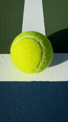 Neon tennis ball at the junction of crisp white court lines on textured green surface, sharp afternoon shadow and minimalist sports background