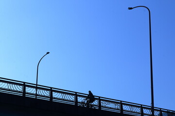 青空を見上げながら陸橋を自転車で渡る人