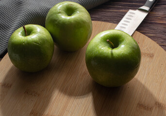 Green apples on a round wooden cutting board with a knife and a blue-gray napkin on one side,  horizontal image