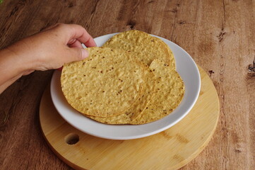 Hands holding corn tostadas to prepare Mexican food on a rustic wooden table. Horizontal image with angle of view.