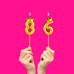 Birthday on a fuchsia background with the number 86 - Hands holding number-shaped candles
