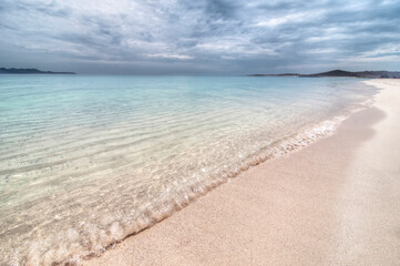 Beautiful white sand beach with calm sea and crystal clear turquoise water with clouds in the sky and mountains in the background seascape of La Paz, Mexico. El Tecolote beach.