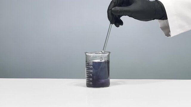Stirring black dye in beaker with glass rod