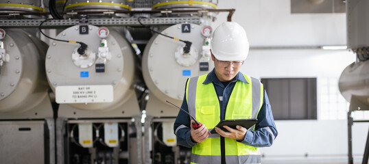 Male engineer inspection of high-voltage gas-insulated switchgear, ensuring safety, control, and precision, wearing safety helmet and reflective vest using a tablet and walkie-talkie