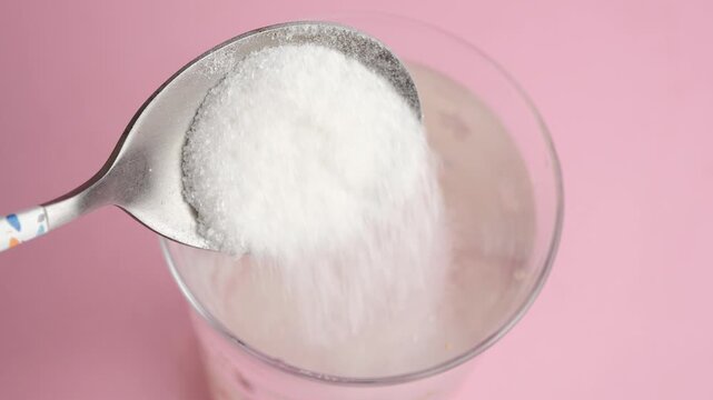 Pouring sugar into a glass of water 