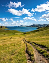 Scenic dirt road winds through grassy hills to a tranquil lake under a vibrant sky