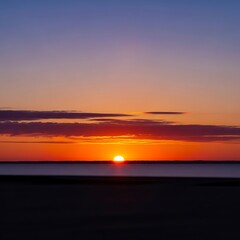 Obraz premium A breathtaking sunrise paints the sky in vibrant hues of orange, purple, and blue over a calm body of water.