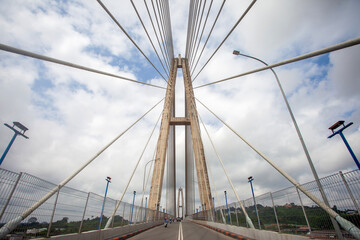 A dramatic, low-angle view of the main pylon and cable-stayed construction of the Mahkota II Bridge in Samarinda, Indonesia. Passing motorcycles provide scale to the massive structure