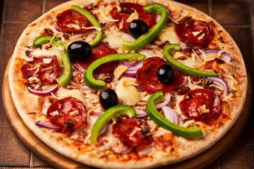 Pizza with chorizo ​​sausage, mozzarella cheese, green pepper and black olives. Rustic wooden background. Soft focus.	