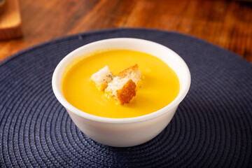 Carrot and pumpkin cream soup. Easy, nutritious and healthy homemade recipe. Served in a white bowl with bread croutons. Perfect to accompany everyday food.