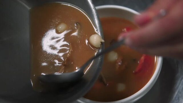 Preparing asian soup. Pouring meal. Chef hand serving hot dish of octopus shrimp squid mushrooms. Liquid spicy tomato broth ladling to bowl.