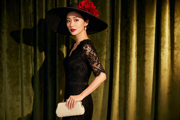 east asian woman exuding elegant retro charm in a black lace dress, wearing a wide-brimmed hat adorned with red flowers and holding a pearl clutch.Generated by AI