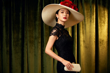 east asian woman exuding elegant retro charm in a black lace dress, wearing a wide-brimmed hat adorned with red flowers and holding a pearl clutch.Generated by AI
