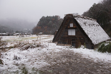 Shirakawa-go, Gifu, Japan: A historic Gassho-zukuri style farmhouse stands in a gloomy, snow-covered landscape during the first snowfall of the winter season.