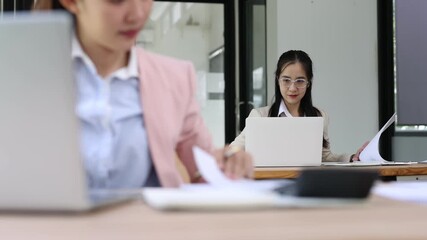Young business woman reviewing financial documents and using calculator while sitting at her desk in office.