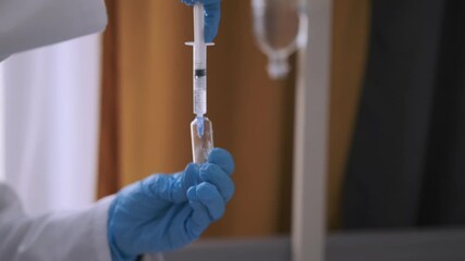 Young nurse in mask and gloves fills syringe with medicine from vial to prepare IV drip injection. Patient resting in hospital bed during treatment procedure. - Powered by Adobe