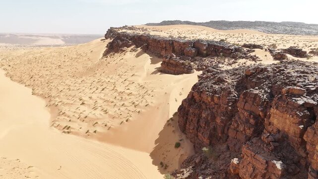 Aerial drone view of golden Sahara desert dunes meeting dark rocky cliffs in Mauritania, dramatic contrast of sand and stone in the remote wilderness