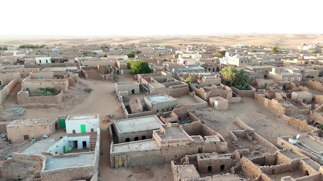 Aerial drone view of Chinguetti Old Village desert oasis in Mauritania with palm groves, farmland and traditional houses surrounded by endless golden Sahara sands