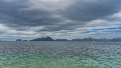 The surface of the calm turquoise ocean. Ripples on crystal clear water. A white sailing yacht in the distance. Mountains on the horizon. Clouds in the sky. Philippines. Palawan.