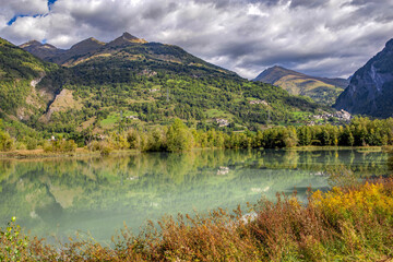 blue turquoise mountain lake in mountainous landscape bordered by colorful vegetation in autumn in french alps