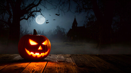 Halloween pumpkins on wooden table in front of haunted house at night