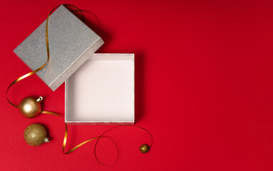 Top view of gift box with lid, golden ribbon and baubles on red. Clean Christmas copy space template for sale and promotion.