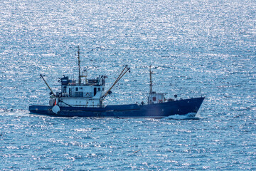 Fishing boat in blue sea and clear sky with birds flying overhead.