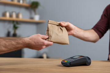 Hands giving a paper bag for takeout service with payment terminal