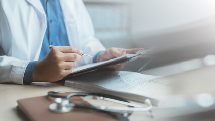Fototapeta premium Doctor writing medical notes on a clipboard with a stethoscope on the desk, symbolizing healthcare consultation, diagnosis, treatment, and professional medical service.