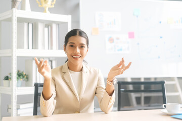 Fototapeta premium Portrait of young adult southeast business woman with smile teeth confident wearing white suit sitting in office