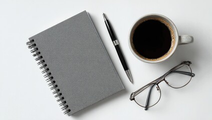 Flatlay of gray spiral notebook, pen, coffee, and eyeglasses on white background