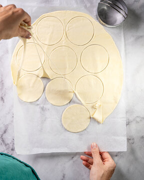 Pastry dough preparation on marble &mdash; round cut-outs for pies with hand removing excess dough, clean high key food styling with copy space.