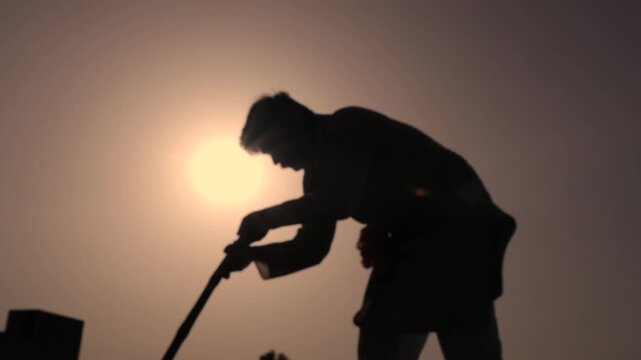 Silhouette of Indian farmer digging farmland with shovel working hard in agriculture field for his better future and hope for good crop. Summer time. Rural india. Copy space.
