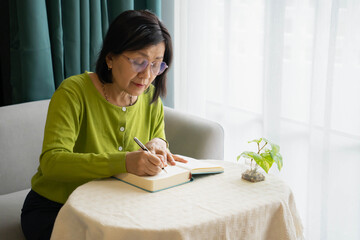Mature Asian Woman Writing Daily Diary at Home for Personal Reflection.